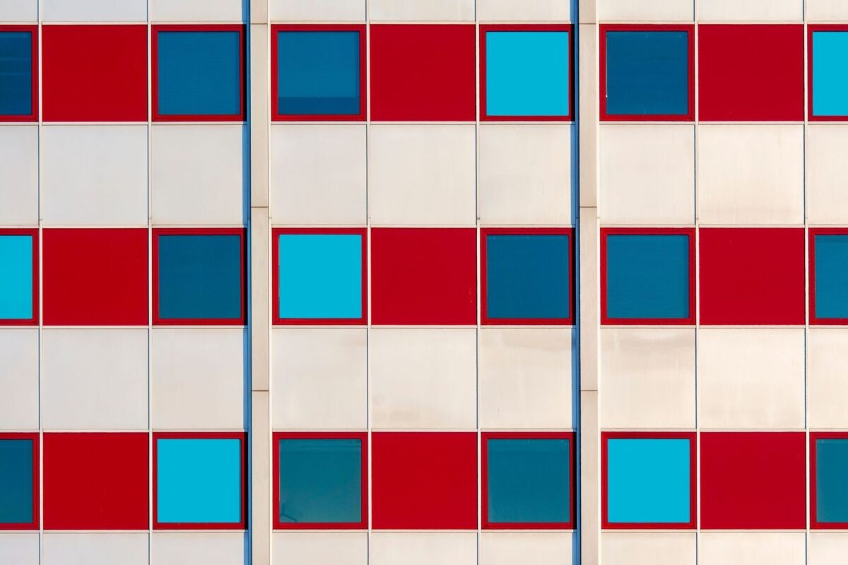 Geometric building facade with a repeated grid of red panels and blue windows