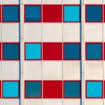 Geometric building facade with a repeated grid of red panels and blue windows