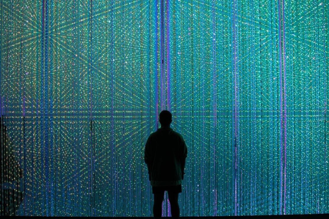 Silhouette facing a wall of colorful, grid-like digital lights